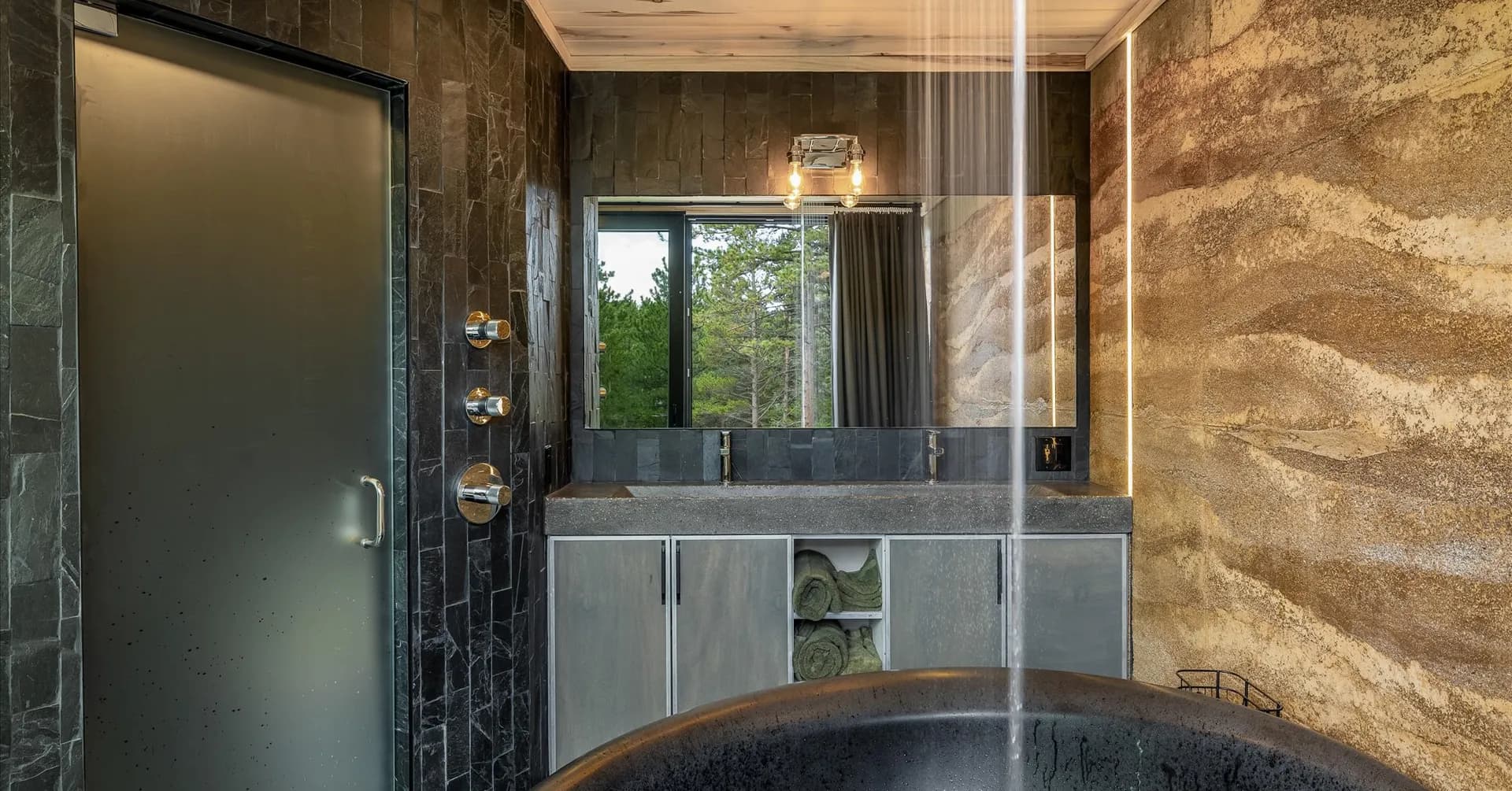 Rammed earth wall and slate tile thi bathroom with an oversized soaking tub and rainfall showerhead